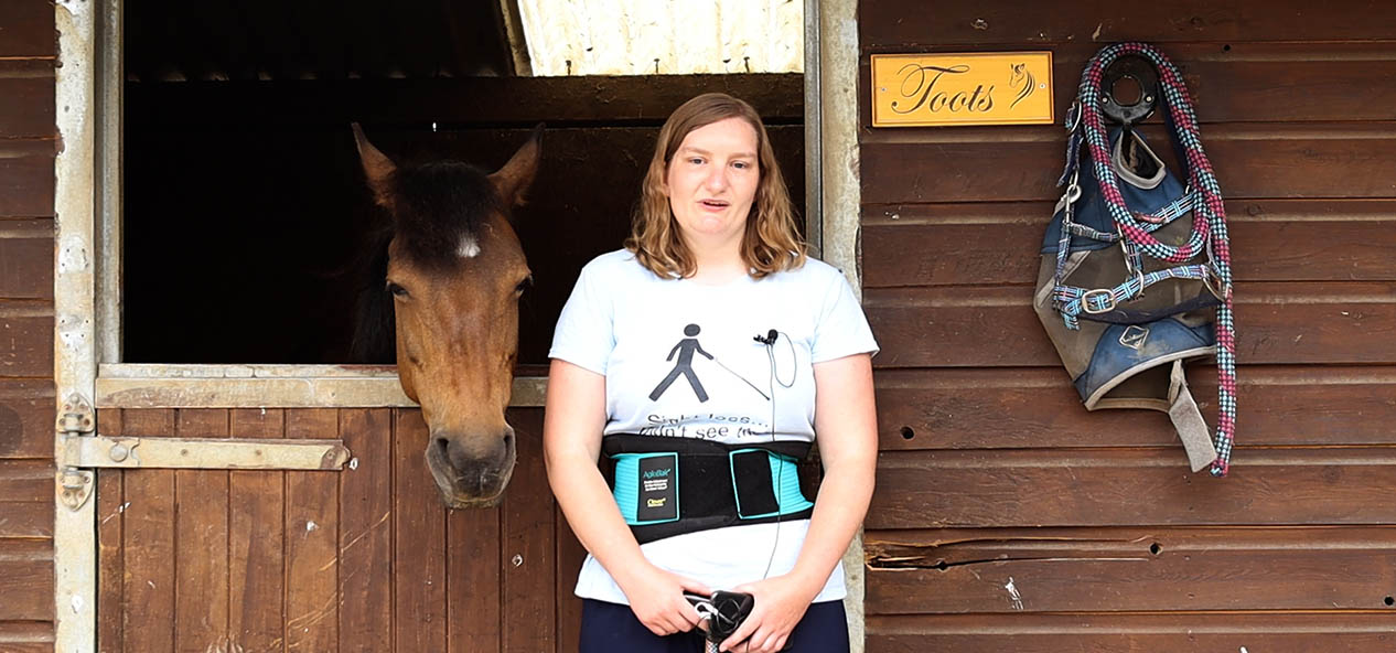 A woman wearing a back support poses outside a stable with a horse called Toots