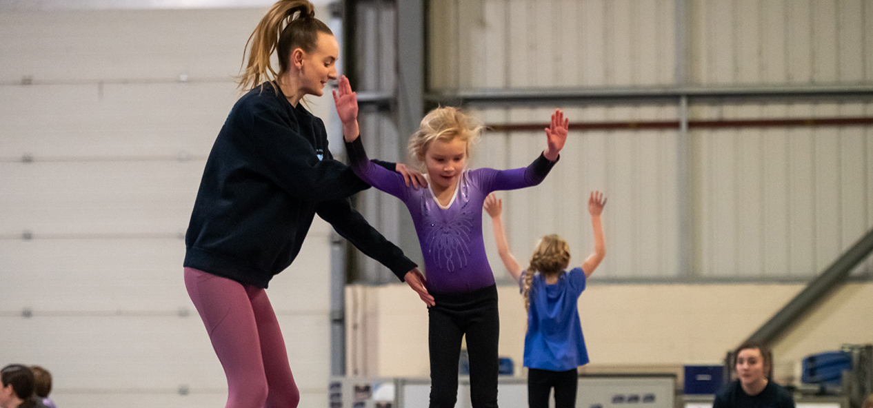 An instructor helps a young girl in a gymnastics class