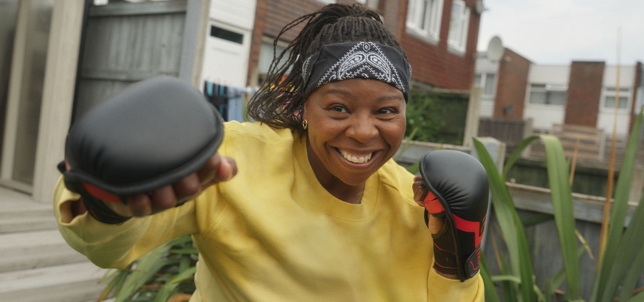 A woman wearing boxing training gloves poses, in her garden, as if she's about to punch the camera