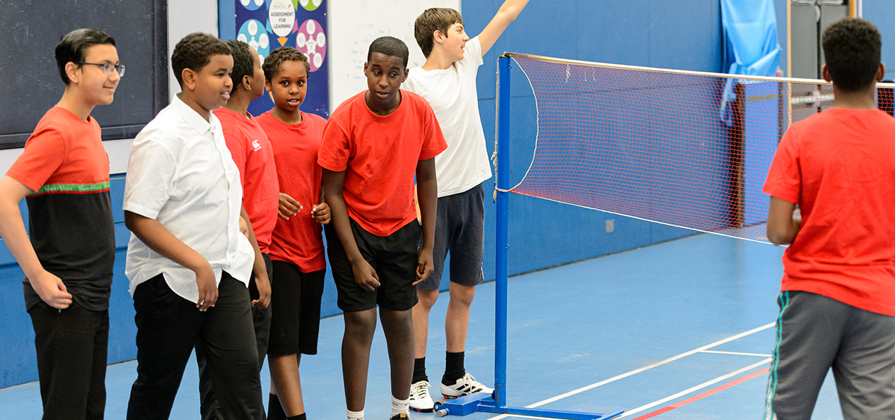 A small group of kids stand by a badminton indoors pitch.