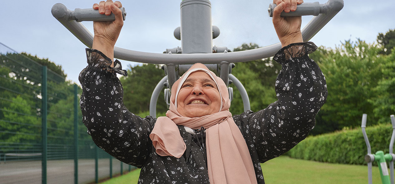 A woman wearing a head scarf uses a shoulder press machine in a park gym