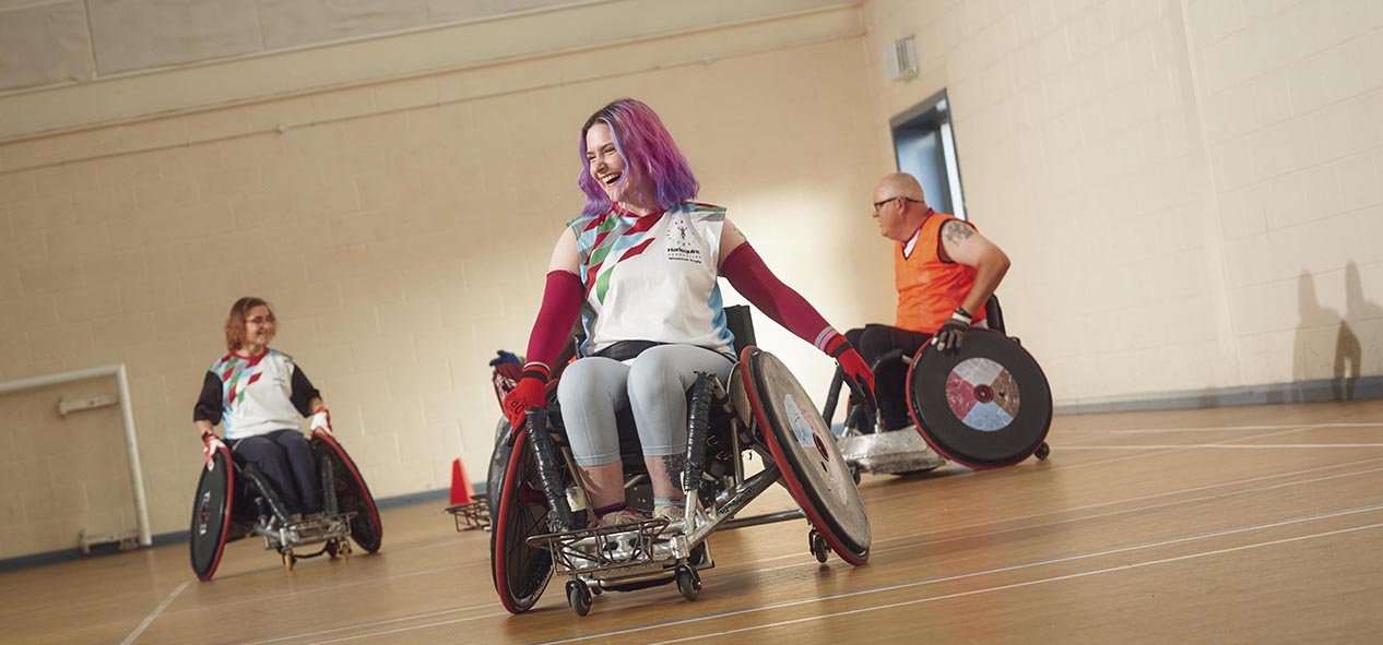 Three people in wheelchairs play wheelchair rugby