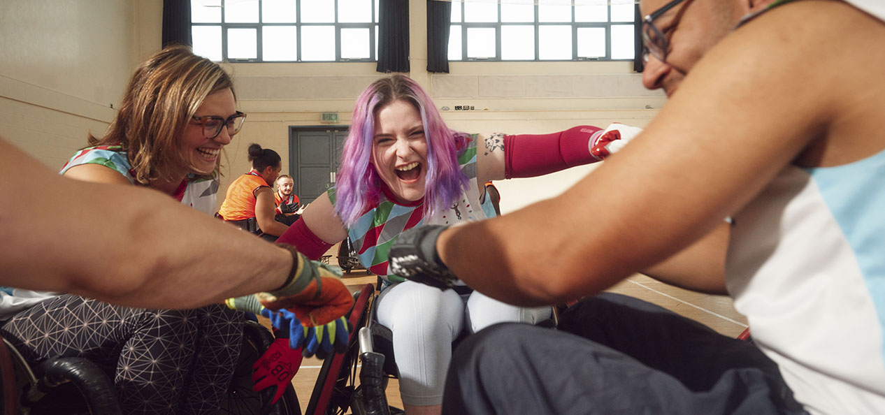 Three wheelchair rugby players arrange themselves in a circle and put their hands together to prepare for a match