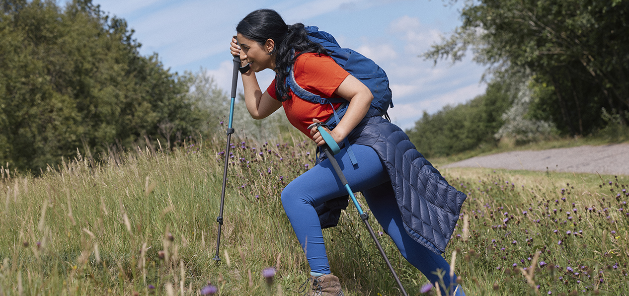 A South Asian woman walks up a hill using walking poles