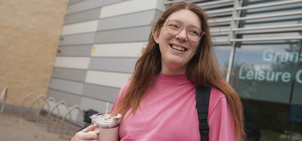 A pregnant woman holding a flask of water smiles outside a leisure centre