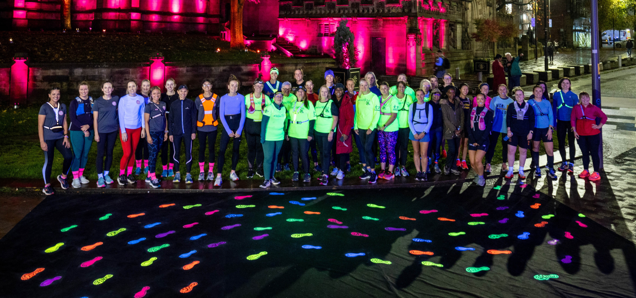 Runners pose in front of glow-in-the-dark footprints at night in Manchester.