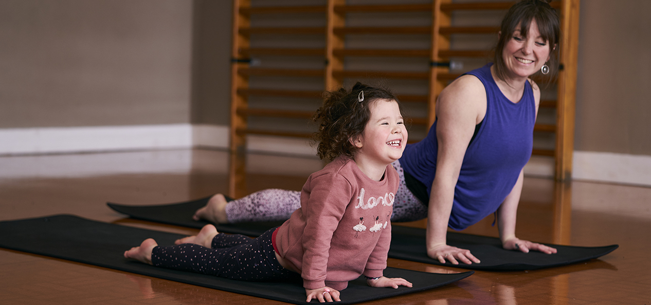 A smiling mother and daughter practice yoga together, side by side