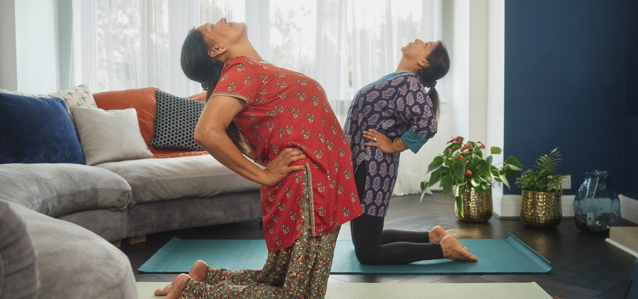 Two women stretch on their knees during a living room yoga session.