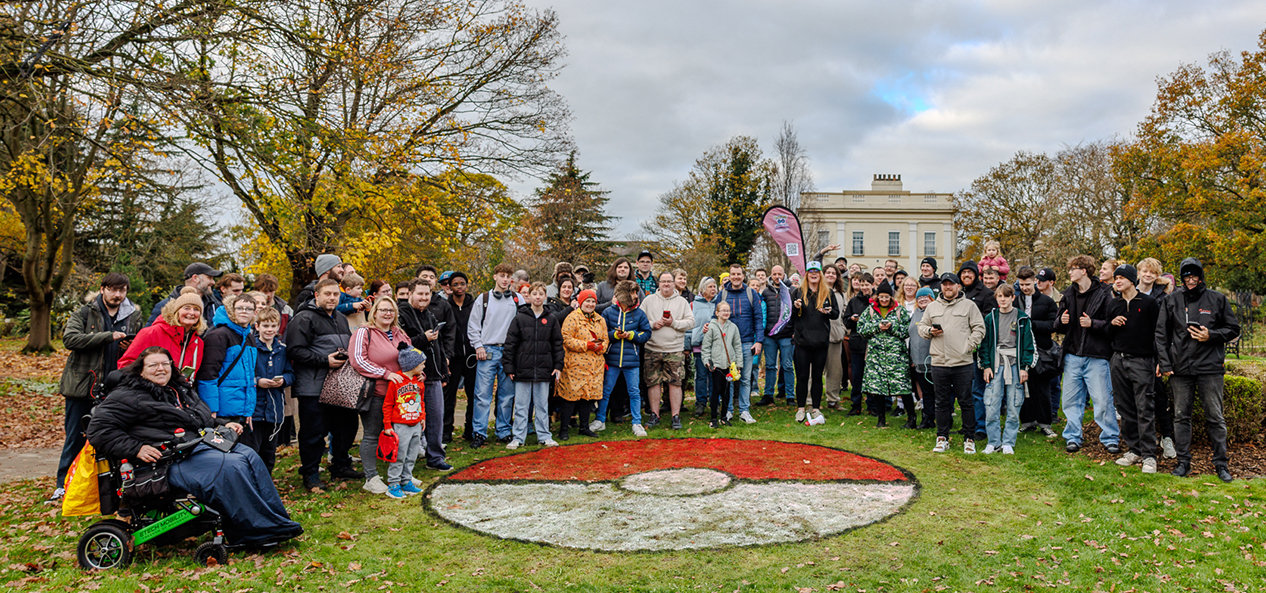 A group of poeple pose around a Pokemon ball that's been painted on park's floor. 
