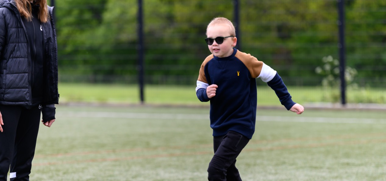 A boy wearing dark glasses runs on an outdoor artificial pitch.