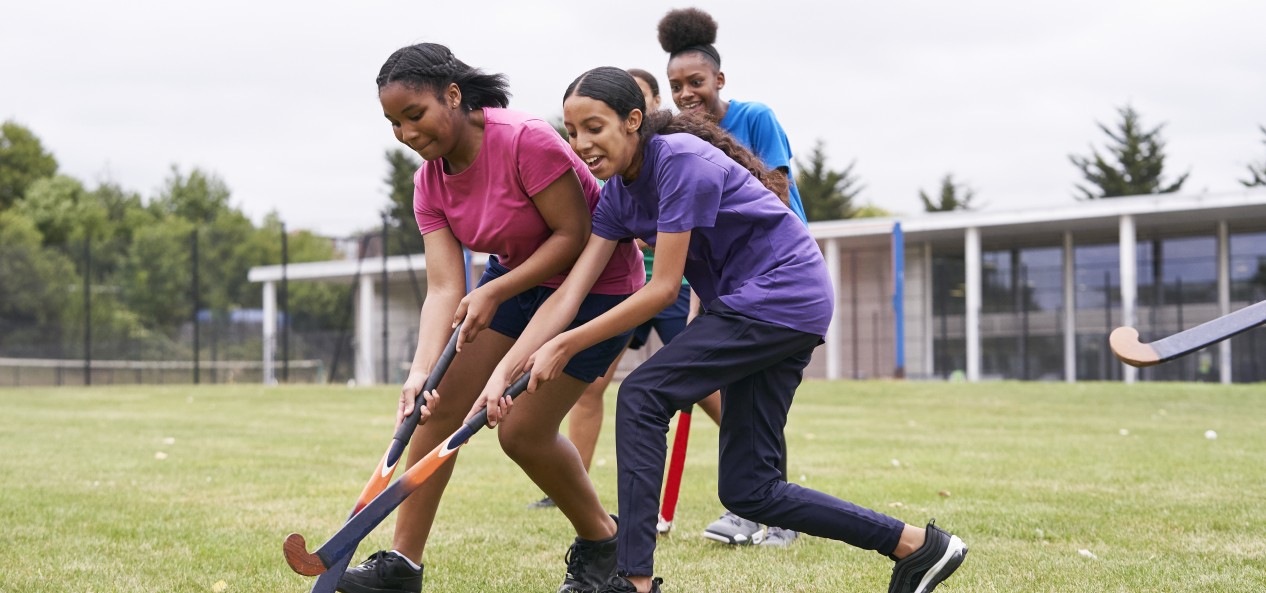 Two girls contest the ball during a game of hockey on a grass pitch.