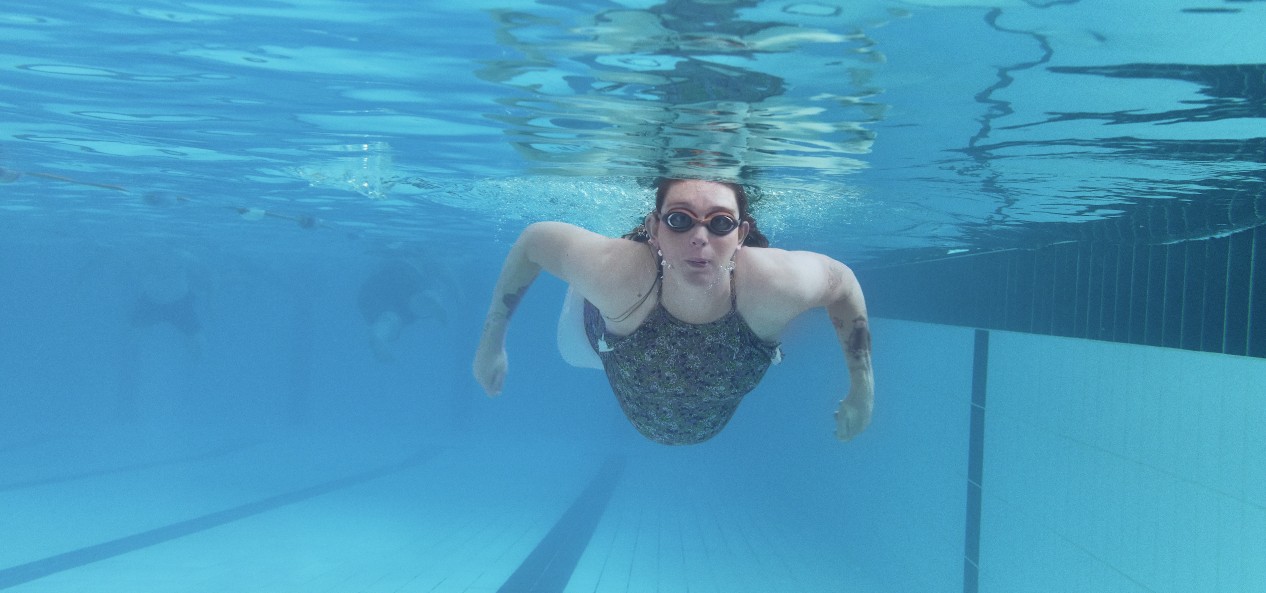 A pregnant woman wearing goggle swims under water in a pool.