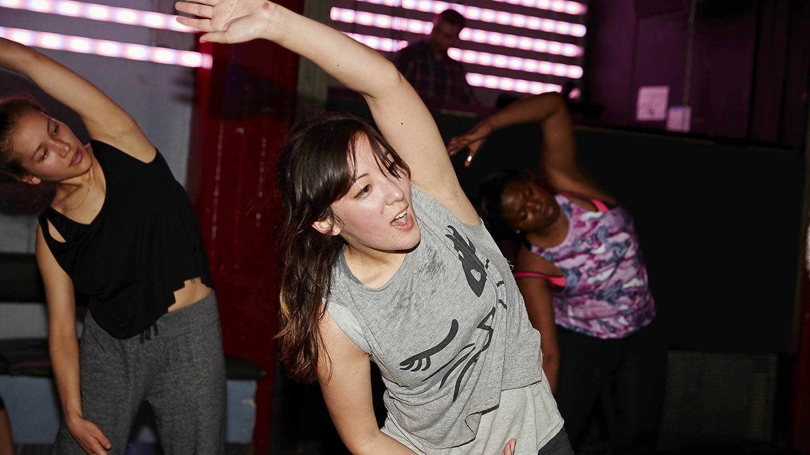 Women stretch their arms over their head during an exercise class in a studio.
