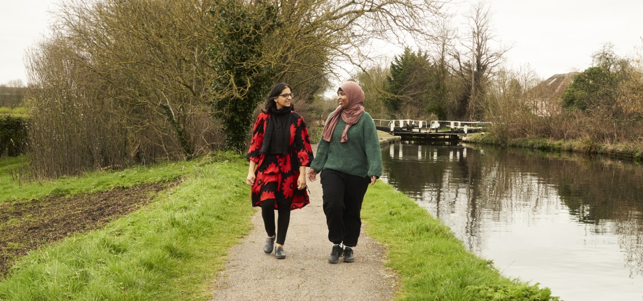 Two women of South Asian descent walk side by side down a canal towpath.