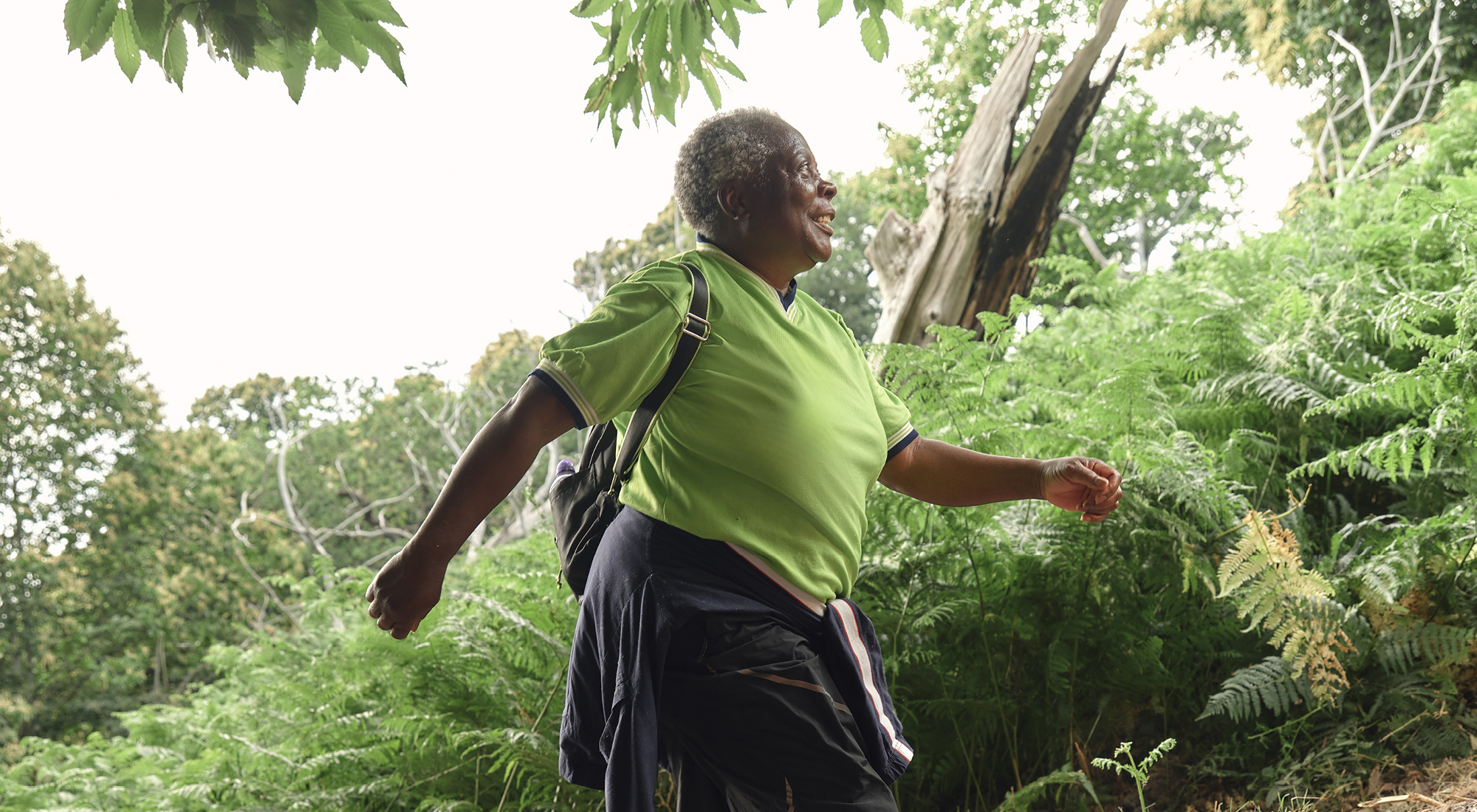 Picture of a black woman, in a green t-shirt, walking in the woods