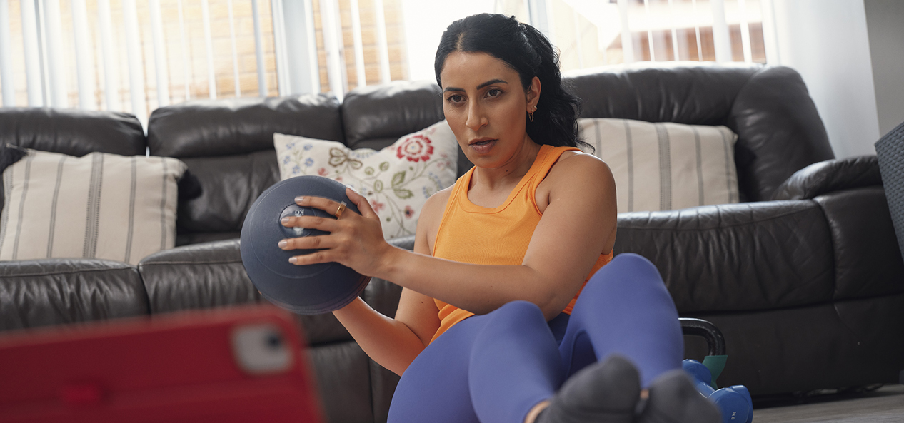 A woman uses a medicine ball to perform Russian twists during a home exercise session