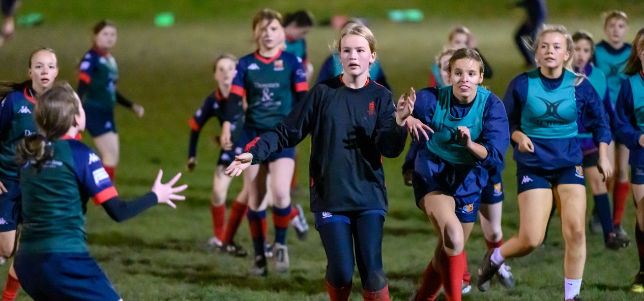 A group of girls play rugby on a field at night.