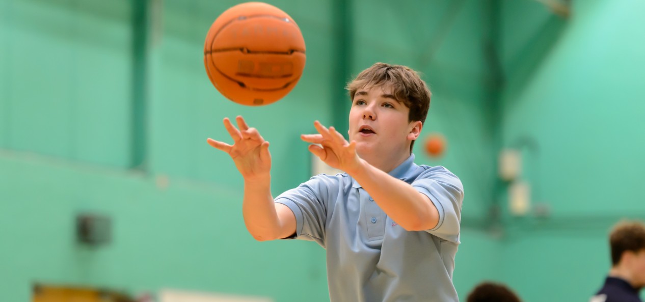 A schoolboy throws a basketball in a school hall.