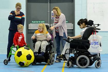 Two child wheelchair users and a and a boy with a walking frame play with a giant football