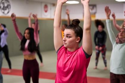 Women in an exercise class raise their arms to the ceiling of the sports hall