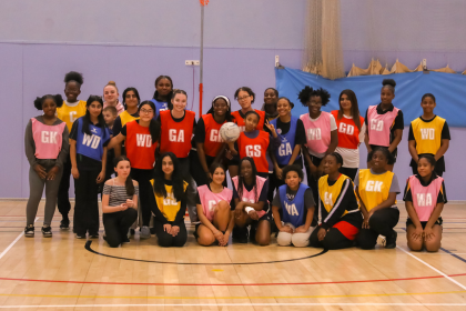 Girls  in their Netball Bibs take a group picture in sport hall