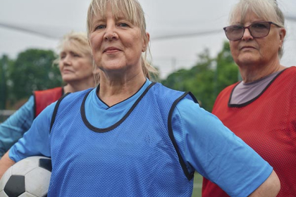 Three female walking football players pose for a photo, with hands on their hips and one of them holding the ball under their arm