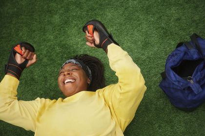 A woman lies on the grass, laughing, wearing boxing training gloves