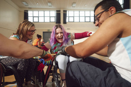 Three wheelchair rugby players arrange themselves in a circle and put their hands together to prepare for a match