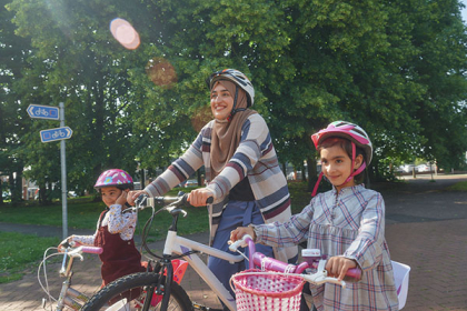 A woman and her two daughters all ride their bikes in a park