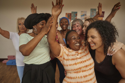 A woman smiles as she dances with a group of other women in a studio