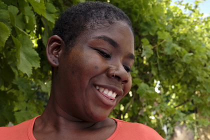 A head and shoulders photo of a smiling black woman with short cropped hair, wearing a coral coloured t-shirt