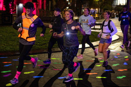 A group of women run at night down a road decorated with high-vis footprints.