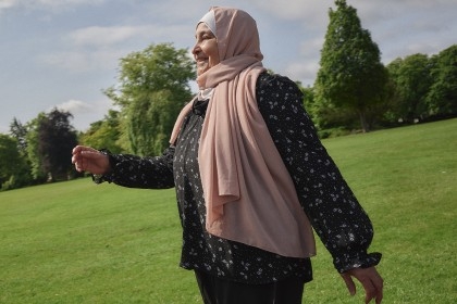 A woman wearing a headscarf walks in a park.