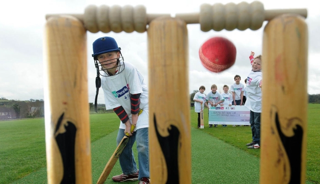 young boys playing cricket and holding giant cheque