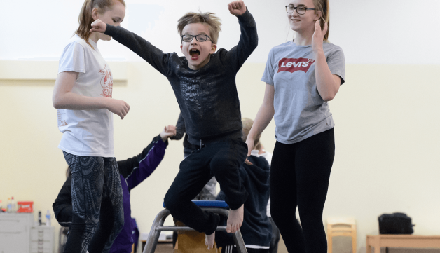 Boy jumping on small trampoline with two girls helping
