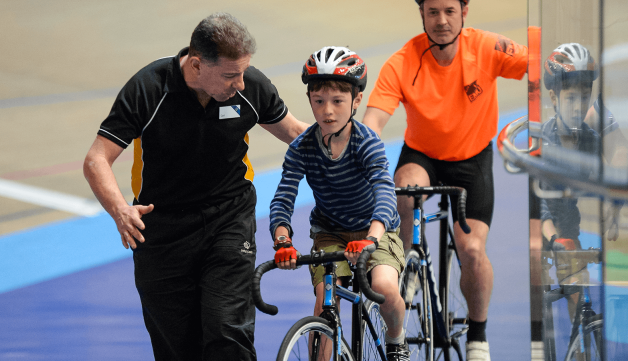 Coach helping young boy cycling on velodrome