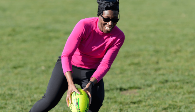 A woman smiling while playing rugby.