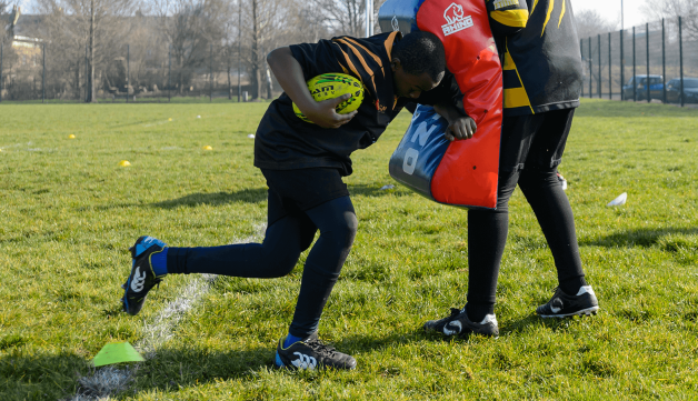 Young boy practicing american football tackle using cushion