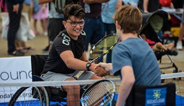 Two boys playing wheelchair tennis shake hands at the net