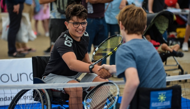 Two boys in wheelchairs shaking hands over a tennis net