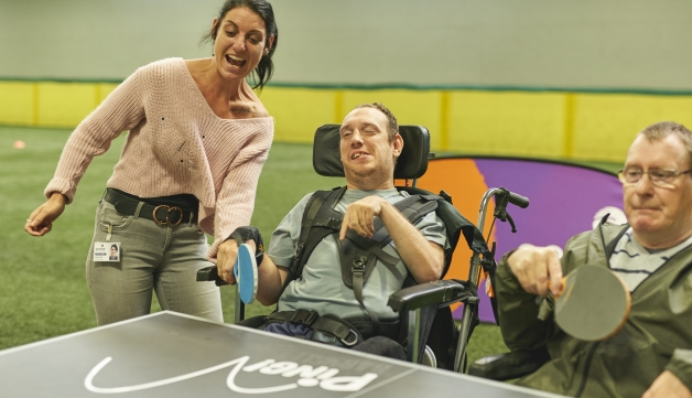 able-bodied woman playing ping-pong with two men in wheelchairs