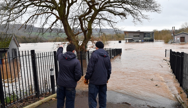 Two men survey the scene of a flooded sports pitch and pavilion