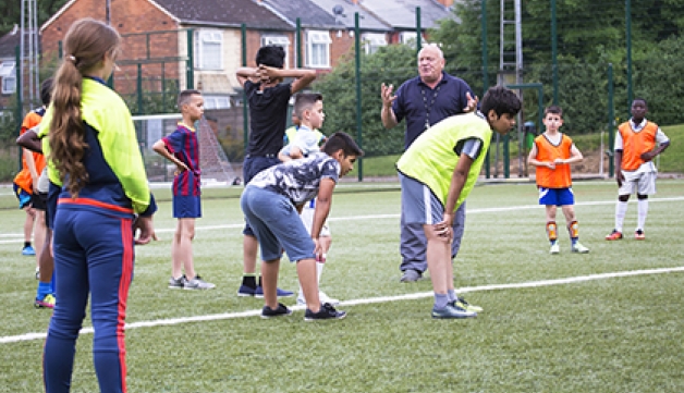 A coach instructing a group of children on a playing field.