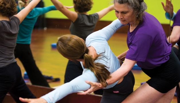 A woman helps another with a pose in a yoga class