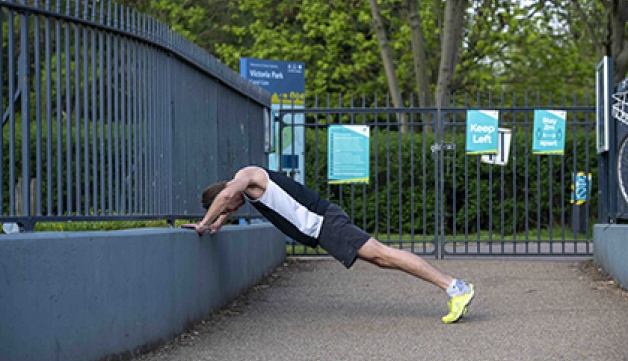 A man leans on a wall outside a park to stretch