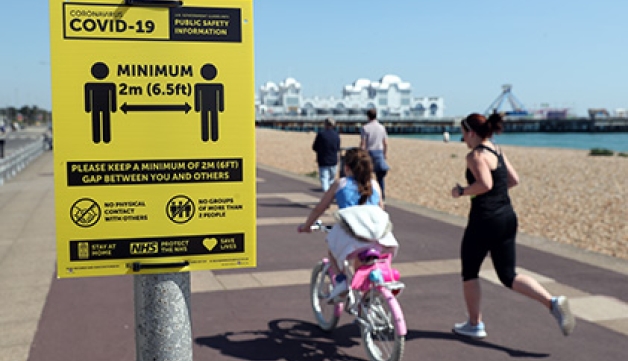 People exercise along Southsea seafront, running and riding past a sign warning about social distancing.