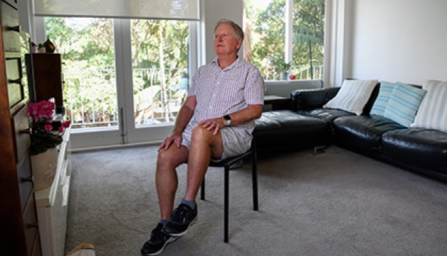 An older man performs seated exercises at home.