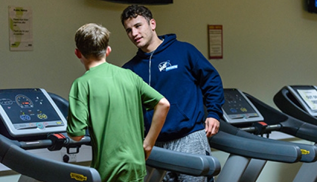 A Street Games volunteer instructs a boy how to run on a treadmill