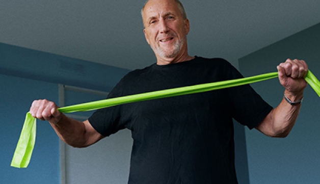 A man performs exercises at home using a resistance band.