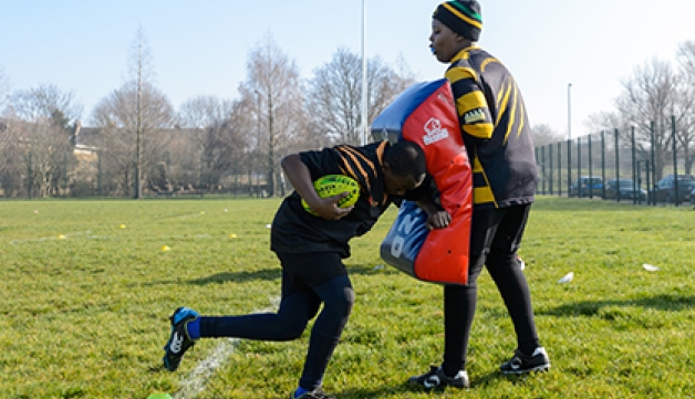 Two rugby players perform a tackling drill with one holding a tackling pad